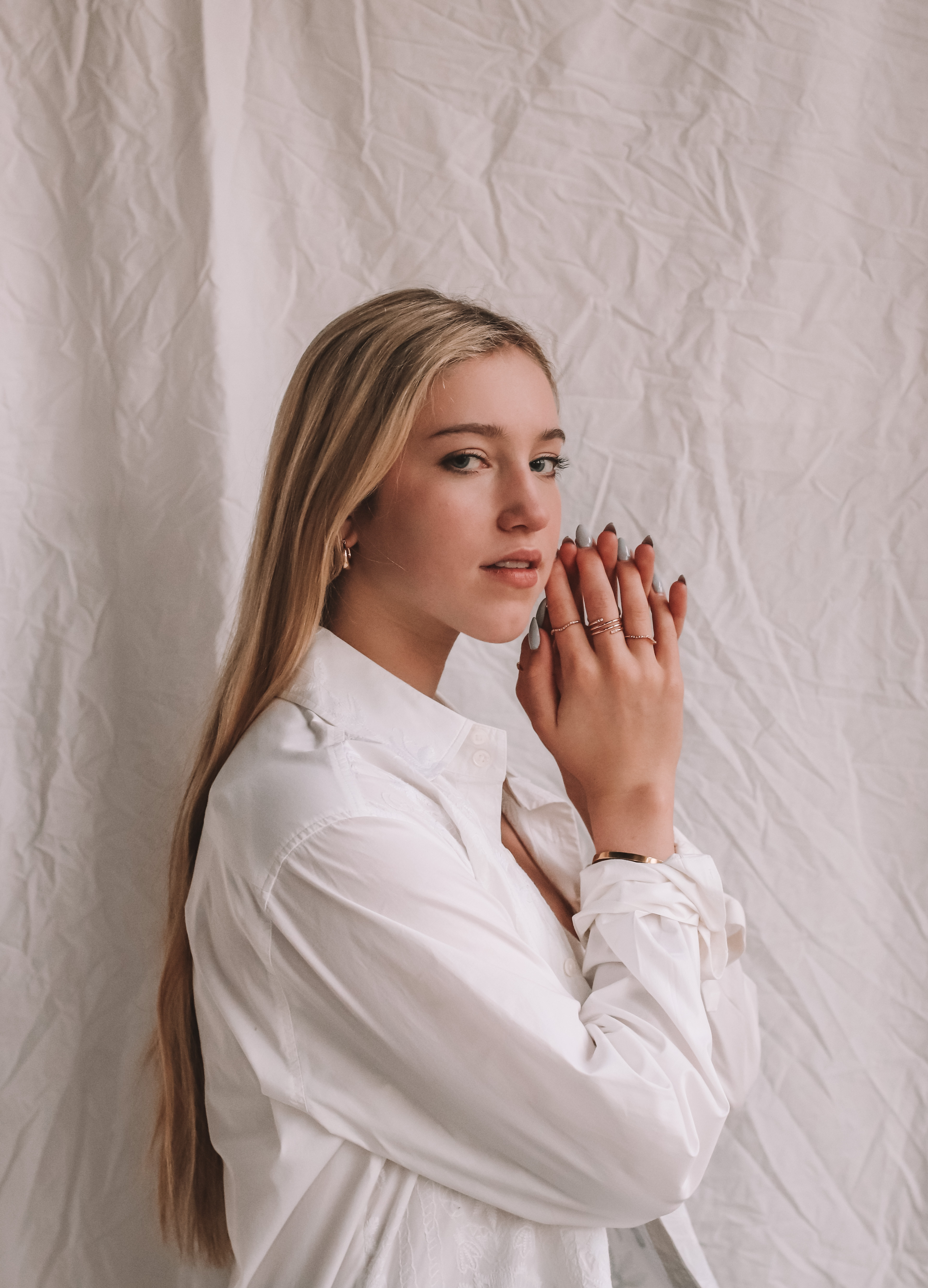 editorial photo of a girl with blonde hair wearing a white button-down and gold jewelry resting her face on her hands