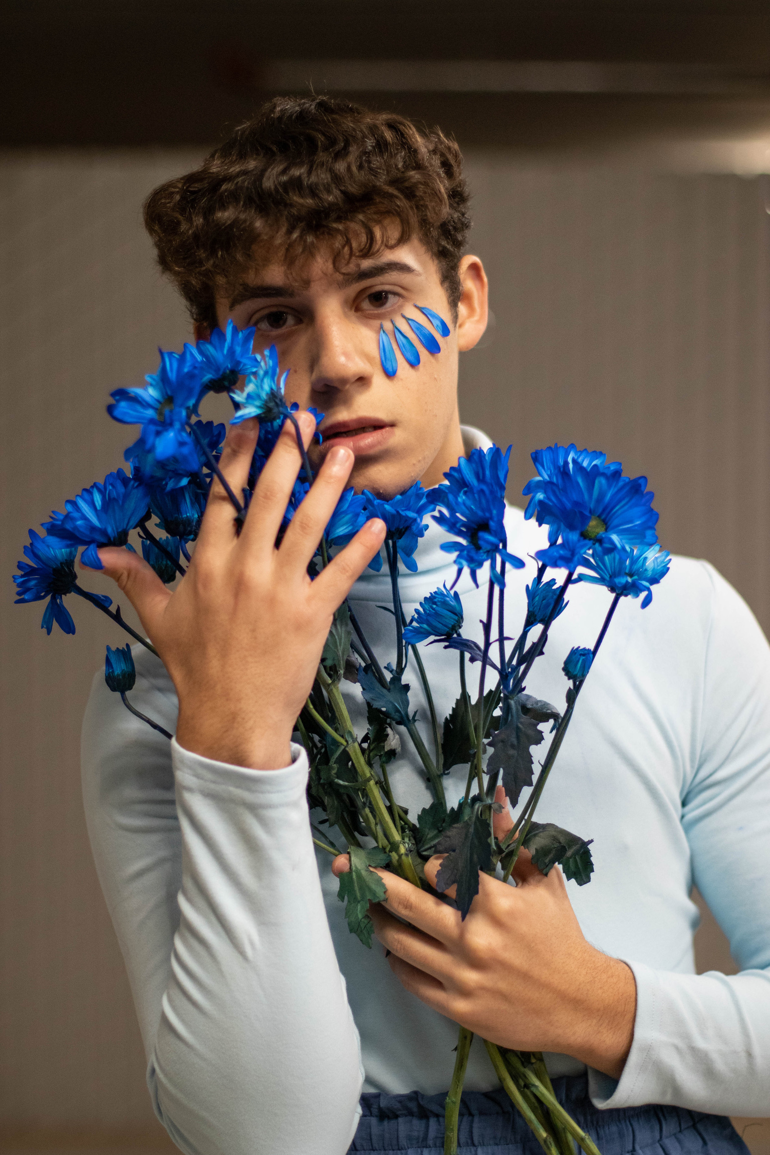 boy with brown hair wearing a light blue turtleneck, framing his face with vibrant blue flowers