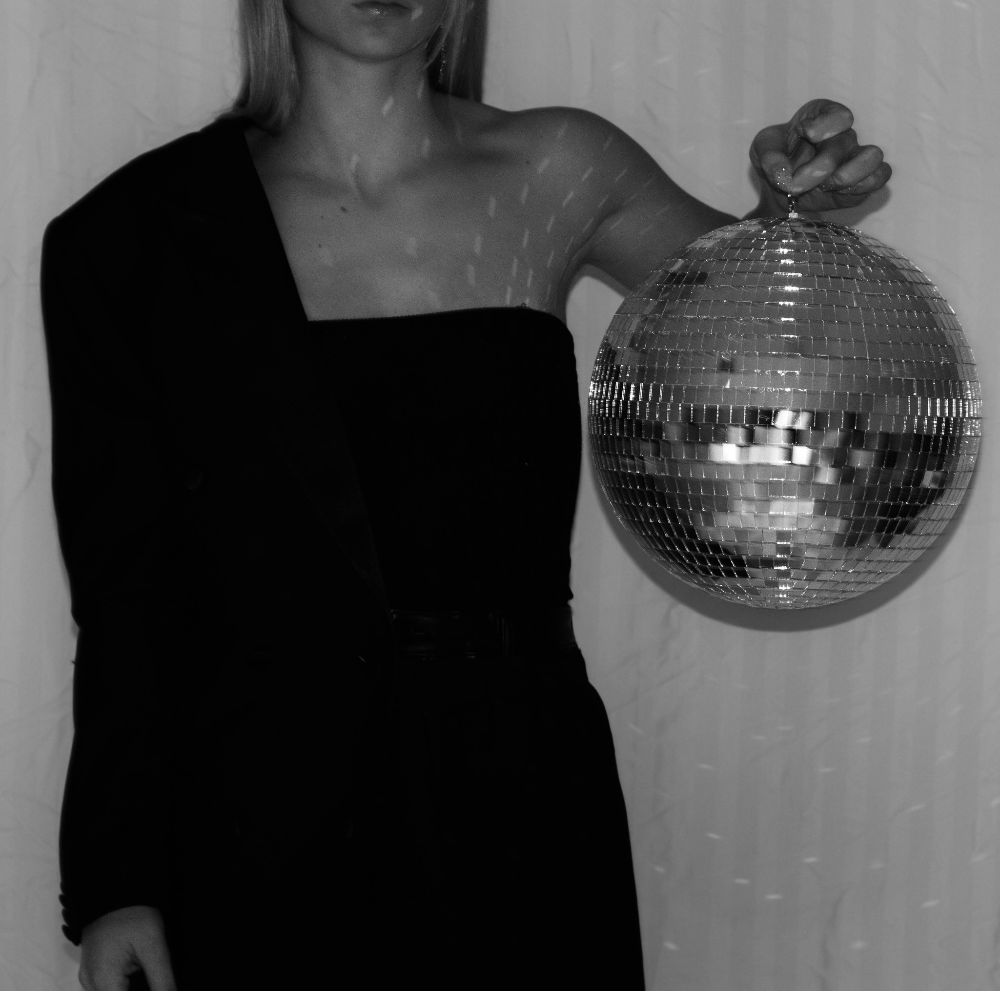black and white editorial image of a girl wearing half of a suit jacket while holding a disco ball