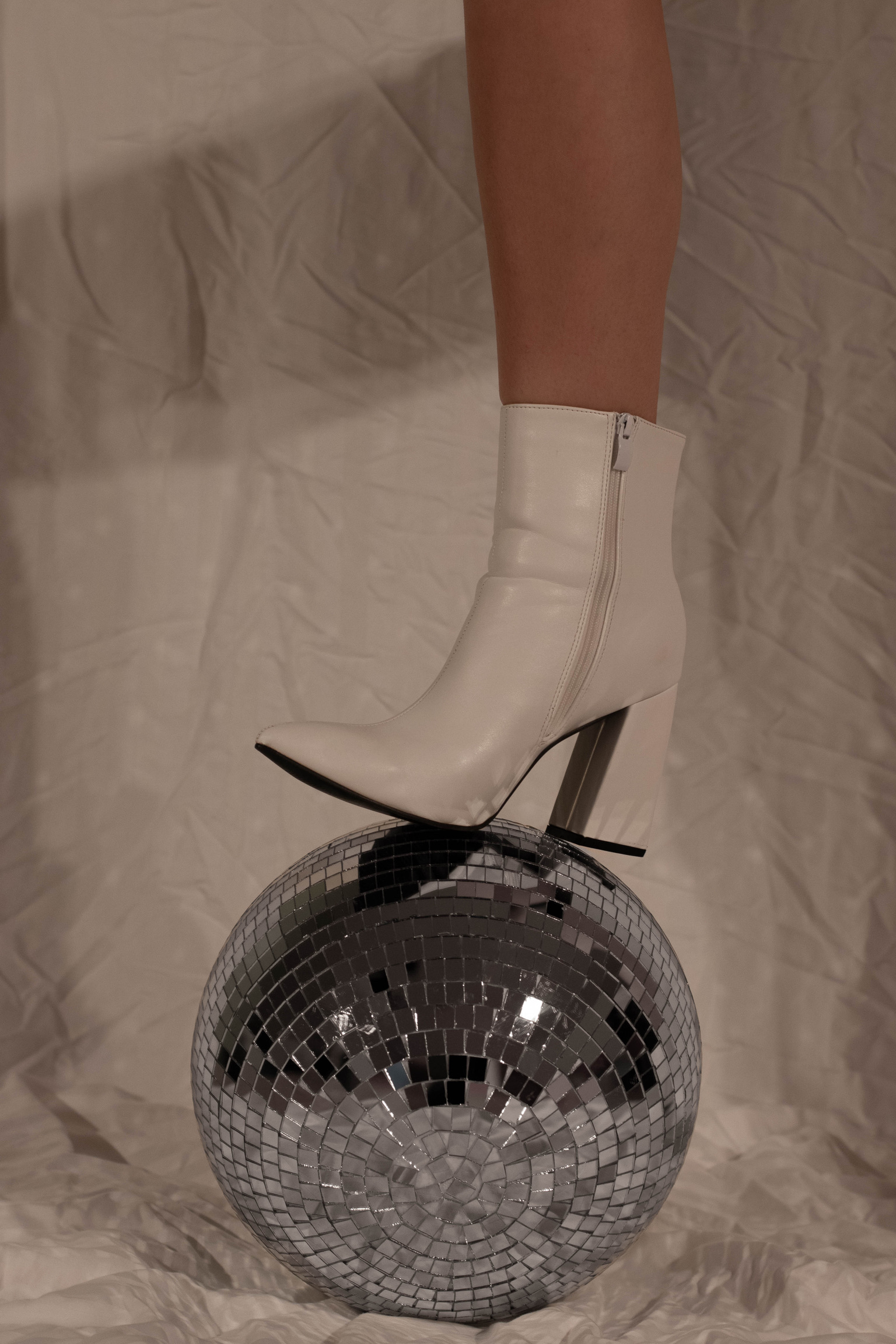 editorial photo of a disco ball and a girl wearing white boots stepping on the ball with one foot